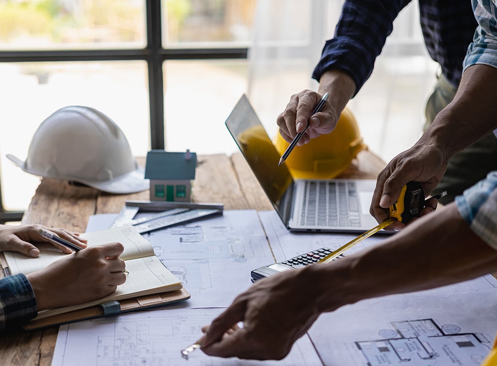 Builders reviewing house plans, a laptop and a calculator with hard hats on the table